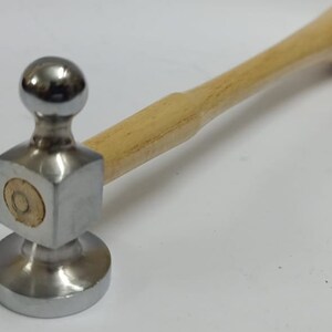 May include: A metal ball-pein hammer with a polished steel head and a light-coloured wooden handle. The hammer's head has a rounded striking surface and a square face. The handle is smooth and ergonomic.