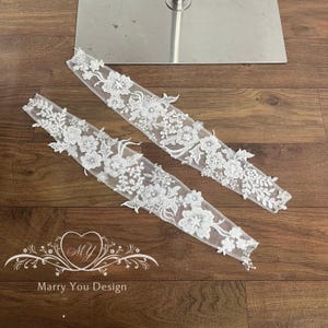 Puede incluir: Dos apliques de encaje floral blanco con intrincados dise&ntilde;os de flores y hojas. Los apliques est&aacute;n colocados sobre una superficie de madera. El texto "Marry You Design" es visible en la parte inferior de la imagen.