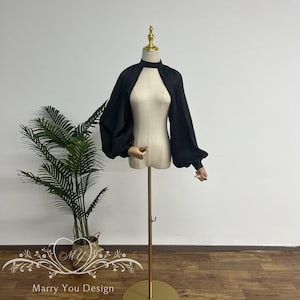 May include: Black sheer fabric shrug with long, puffy sleeves. The shrug is open in the front and has a high neckline.