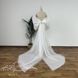 May include: A white wedding dress with a large bow at the back. The dress is made of tulle and has a long train.