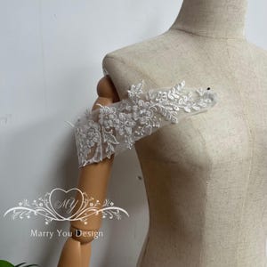 Puede incluir: Manga de novia de encaje blanco con bordado floral y de hojas. La manga est&aacute; sujeta a un brazo de maniqu&iacute;. El texto "Marry You Design" es visible en la parte inferior de la imagen.