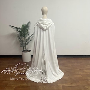 May include: A white hooded cape with a lace trim, displayed on a mannequin. The cape features a long, flowing design with a split in the back and a decorative lace panel. The text "Marry You Design" is visible.