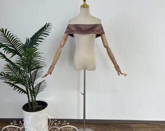 May include: A brown off-the-shoulder satin fabric sash for a wedding dress. The sash is displayed on a white mannequin with wooden arms.