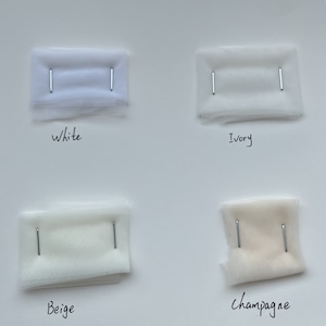 May include: Four fabric swatches of tulle in different shades of white: white, ivory, beige, and champagne. The swatches are pinned to a white background.