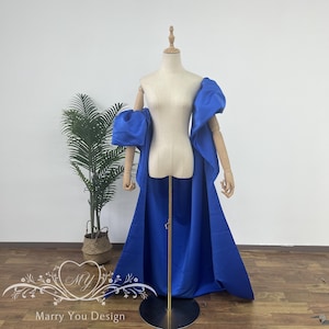 May include: A royal blue dress with large, puffy sleeves and a long train. The dress is on a mannequin and is displayed against a white wall.