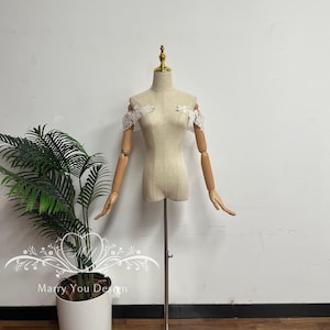 Puede incluir: Un maniqu&iacute; beige con brazos articulados de madera y cuello dorado. Delicada encaje blanco adorna los hombros. El maniqu&iacute; est&aacute; montado sobre un soporte met&aacute;lico. El texto "Marry You Design" es visible en la esquina inferior izquierda.