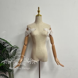 Puede incluir: Un maniqu&iacute; beige con brazos articulados de madera y una parte superior dorada. Delicadas piezas de encaje blanco para los hombros est&aacute;n sujetas al maniqu&iacute;. El texto "Marry You Design" es visible en la esquina inferior izquierda.