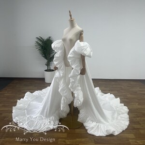 Könnte beinhalten: Ein weißes Brautkleid mit einem dramatischen Design. Das Kleid hat voluminöse, gerüschte Ärmel und einen fließenden Rock mit gerüschtem Saum. Das Kleid wird auf einer Schaufensterpuppe präsentiert, die seine elegante Silhouette zeigt. Der Text "Marry You Design" ist unten sichtbar.