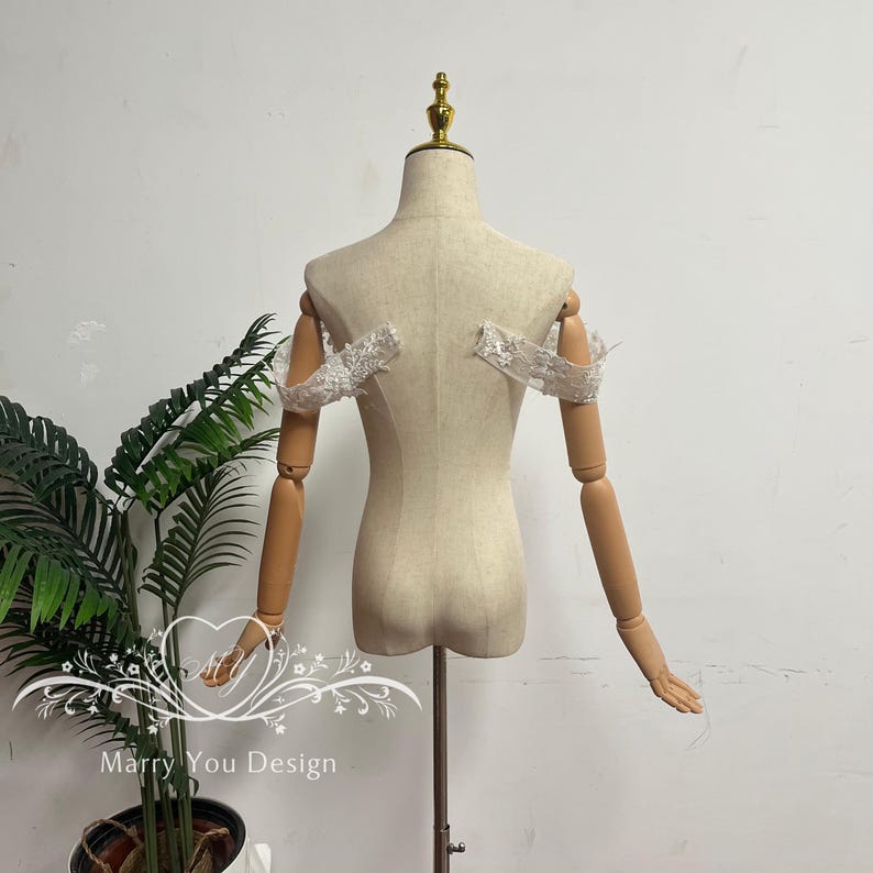 Puede incluir: Un maniqu&iacute; beige con brazos articulados de madera y un remate dorado. El maniqu&iacute; tiene una cubierta de tela y est&aacute; dise&ntilde;ado para exhibir ropa. Mangas de encaje blanco est&aacute;n adjuntas.