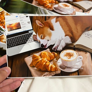 Könnte beinhalten: Ein brauner und weißer Corgi-Hund schläft auf einem Holztisch mit einem Laptop, einem Buch, einer Tasse Kaffee und zwei Croissants. Der Laptop-Bildschirm zeigt einen Sonnenuntergang über dem Meer. Das Buch ist geöffnet und enthält Text auf den Seiten. Die Kaffeetasse ist weiß mit einem braunen Henkel und enthält eine braune Flüssigkeit. Die Croissants sind goldbraun und haben eine flockige Textur.