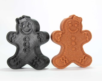 Puede incluir: Un cortador de galletas de hombre de jengibre y una galleta de hombre de jengibre. El cortador de galletas es negro y la galleta es marrón.