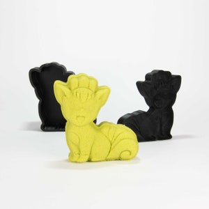May include: A yellow 3D printed figurine of a cartoon fox with a bushy tail. The figurine is sitting on a white surface. There are two black 3D printed molds of the same fox in the background.