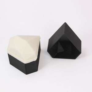 May include: Two black diamond-shaped boxes, one with a white top. The boxes are made of a smooth, matte material.