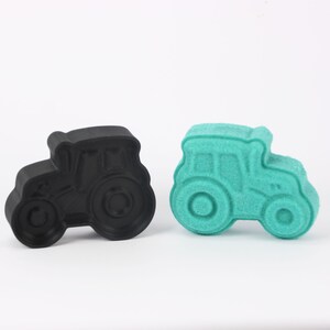 Könnte beinhalten: Zwei traktorförmige Objekte. Eines ist schwarz, das andere türkis. Beide haben ein detailliertes Design eines Traktors mit Rädern, Kabine und Motorhaube. Die Objekte sind wahrscheinlich dekorativ oder neuartig.