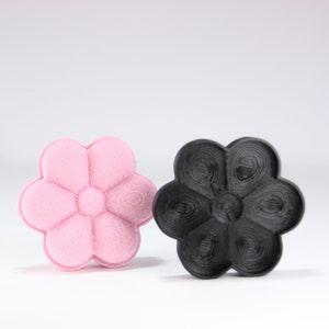 Puede incluir: Dos objetos con forma de flor impresos en 3D, uno rosa y otro negro.