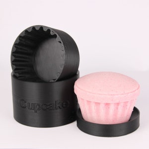 May include: Black cupcake mold with the word "cupcake" printed on the side, and a pink cupcake inside the mold.