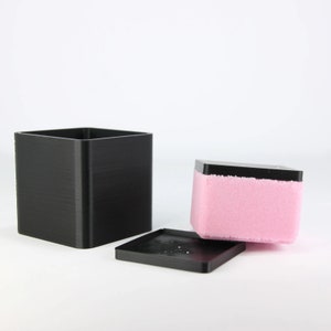 May include: A black square box with a lid and a pink foam insert. The lid is off the box and the foam insert is partially out of the box.
