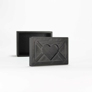 May include: A black wooden box with a heart-shaped design on the front. The box is open and the inside is empty.