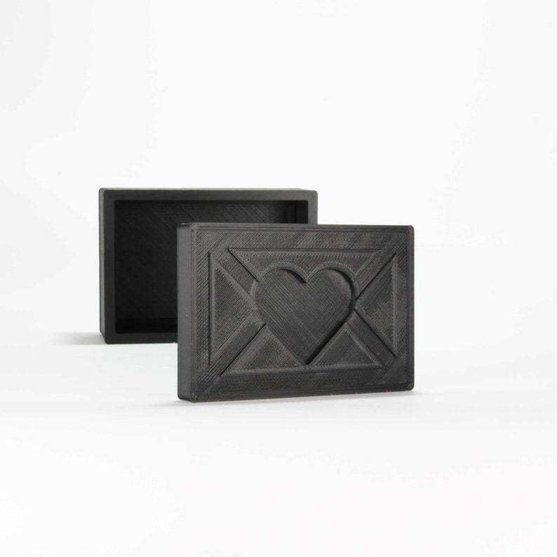 May include: A black wooden box with a heart-shaped design on the front. The box is open and the inside is empty.