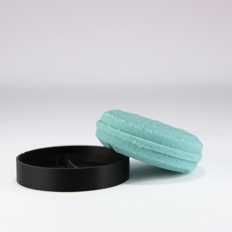 May include: A light blue solid shampoo bar in a black plastic container. The container has a lid that is off and sitting next to the bar.