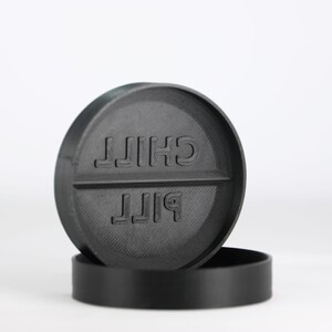 May include: A black pill-shaped coaster with the words "PILL" and "CHILL" printed on it.