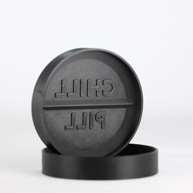 May include: A black pill-shaped coaster with the words "PILL" and "CHILL" printed on it.