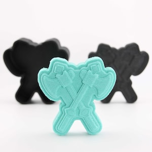 May include: A turquoise blue cookie cutter in the shape of two crossed axes. The cookie cutter is made of plastic and has a smooth surface.