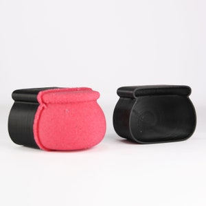 May include: Two cauldron shaped containers, one is black and the other is pink. The pink cauldron has a black rim.