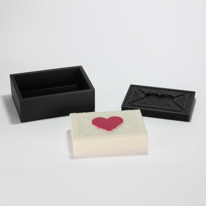 May include: A white box shaped like an envelope with a red heart on the front. The box is open and the lid is black. The lid has a heart-shaped cutout.