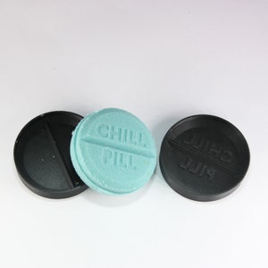 May include: Three round objects, two are black and one is light blue. The light blue object has the words "CHILL PILL" embossed on it. The black objects have the same words embossed on them, but in a different font.