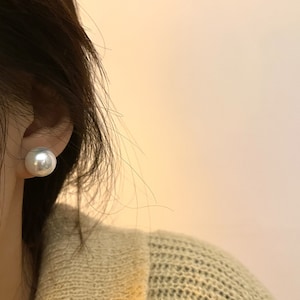 May include: A close-up of a person's ear wearing a large, white pearl earring.