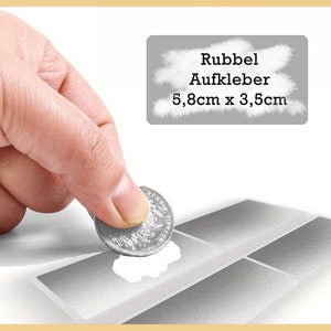Könnte beinhalten: Eine Hand legt eine silberne Münze auf ein Blatt grauer und weißer Klebeetiketten. Die Etiketten sind rechteckig und haben eine strukturierte Oberfläche. Der Text "Rubbel Aufkleber 5,8cm x 3,5cm" ist auf einem grauen Etikett gedruckt.