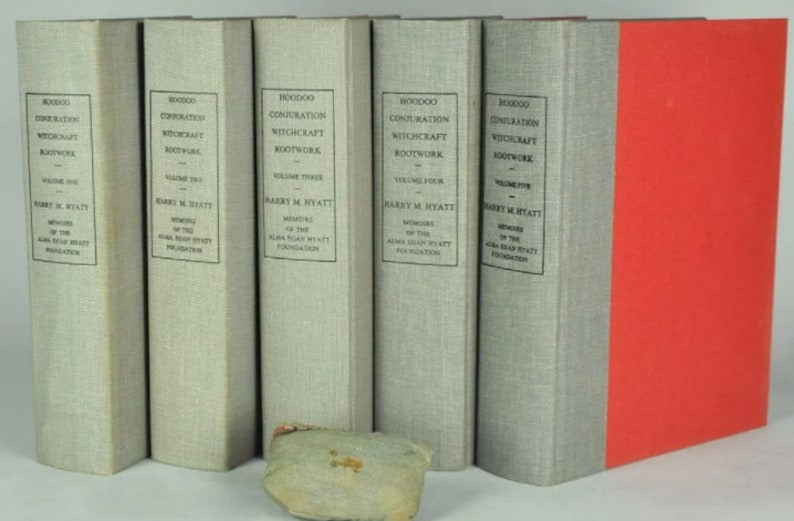 May include: A set of five gray hardcover books with the title "HOODOO CONJURATION WITCHCRAFT ROOTWORK" and the volume number on each book. The books are arranged in order from left to right, with the first book being volume one and the last book being volume five. The last book has a red spine.
