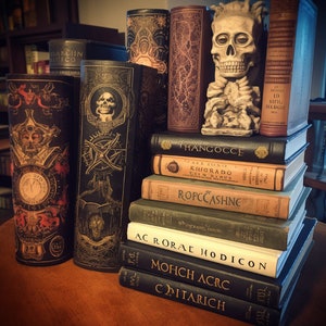 May include: A stack of books with black and gold covers, some with decorative designs. The top book has the title "THANGOCCE" in gold lettering. The books are arranged in a pyramid shape, with the largest book at the bottom and the smallest book at the top.