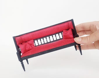 Divano artigianale in miniatura in seta rossa con dettagli neri.