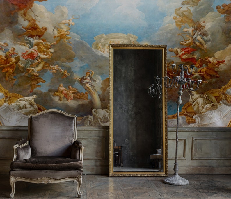 Pu&ograve; includere: Una poltrona in velluto grigio con cornice dorata si trova di fronte a un murale che raffigura una scena di angeli e nuvole. Uno specchio dorato incorniciato di grandi dimensioni e un candelabro in metallo nero si trovano su entrambi i lati della poltrona.