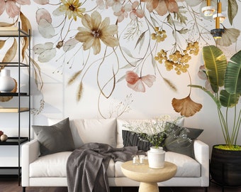 Puede incluir: Un sofá blanco con una manta de tiro gris y una pequeña mesa de madera con un jarrón de flores blancas. La pared detrás del sofá tiene un mural floral de acuarela con flores marrones, rosas y amarillas.