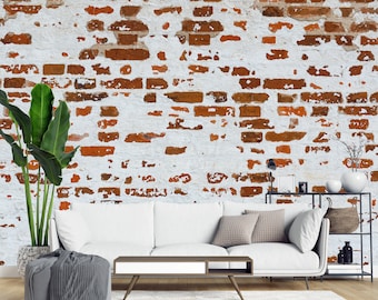 May include: A white sofa with grey throw pillows and a grey blanket sits in front of a white brick wall with red brick accents. A potted plant is on the left side of the sofa and a small table with a lamp and a book is on the right side.