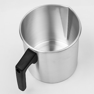Könnte beinhalten: Ein silberfarbener Metall-Gießkrug mit einem schwarzen Griff. Der Krug hat einen Ausguss zum einfachen Gießen und ist zum Schmelzen von Wachs oder anderen Flüssigkeiten bestimmt. Der Griff ist an der Seite des Kruges befestigt.