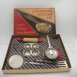 May include: A vintage children's kitchen set in a cardboard box. The box features the text "CHILDREN'S KITCHEN SET" and "USABLE DURABLE Beauty Bright Steel". The set includes a rolling pin, pots, pans, and utensils.
