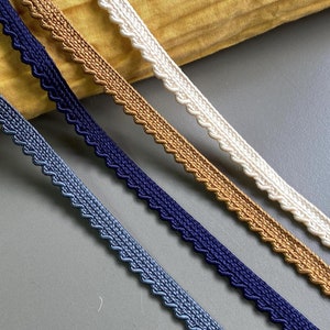 Puede incluir: Cuatro colores diferentes de ribete con un borde festoneado. El ribete se muestra sobre un fondo de tela amarilla.