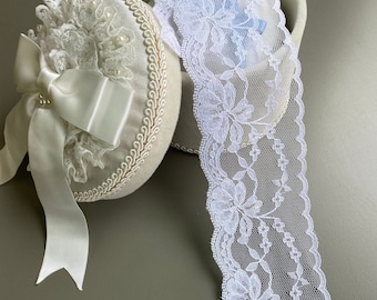 May include: White lace trim with a floral design. The lace is in a round box with a white satin ribbon and bow.