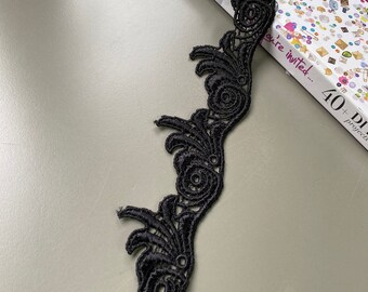 May include: Black lace trim with a floral design. The lace is delicate and intricate, with a scalloped edge.