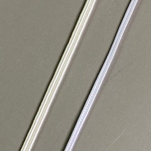 Op de afbeelding: Twee witte satijnen linten, een met een subtiele glans en de andere met een meer uitgesproken glans, liggen op een grijs oppervlak.