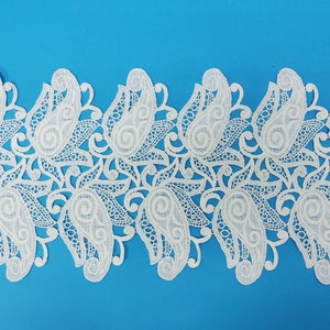 Puede incluir: Borde de encaje blanco con un patrón de paisley. El encaje es delicado e intrincado, con un borde festoneado.