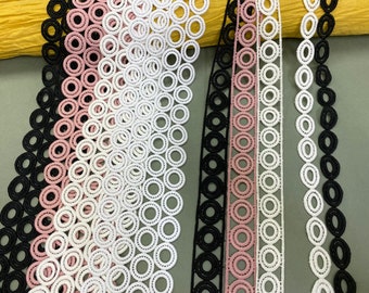 May include: Four different trims of lace with a circle pattern. The trims are black, pink, white, and white with a smaller circle pattern. The trims are all on a green background.
