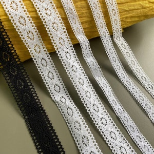May include: Five different lace trims, four white and one black, are arranged on a yellow fabric background. The lace trims have a delicate, intricate pattern.