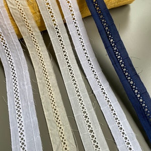 Pode incluir: Cinco rendas de algodão branco com um delicado design vazado, e uma renda de algodão azul marinho com um design semelhante.