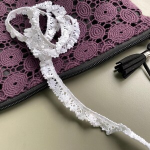 May include: A purple crocheted zippered pouch with a black zipper and a black tassel. The pouch has a white crocheted trim.