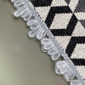 Peut inclure: Un tapis à motifs géométriques noir et blanc avec une bordure à franges. Les franges sont de couleur gris clair.